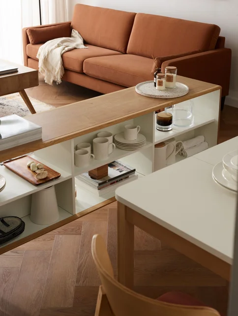 Ruda sofa, komoda w kolorze drewna na tle beżowej ściany
